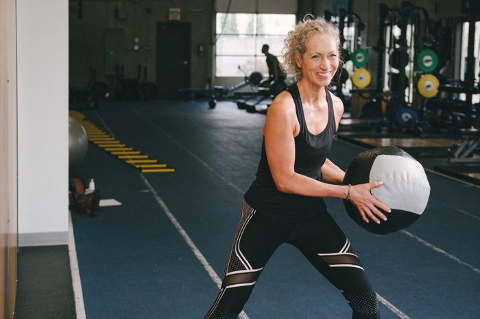 Smiling Woman Exercising With Medicine Ball While At Gym