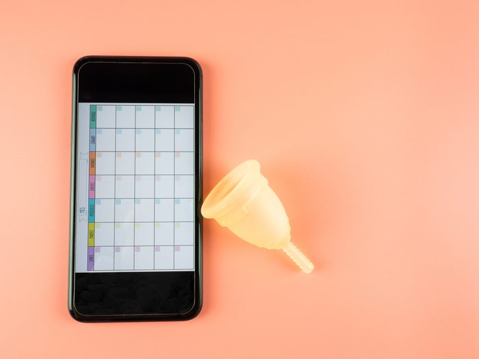 a smartphone with a menstrual calendar mobile app and menstrual cup on a pink background