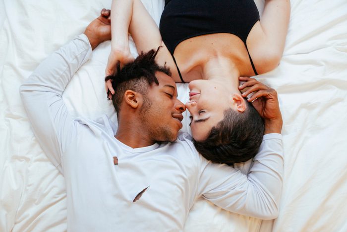 Aerial view of interracial couple of lovers lying on a white bed on a romantic weekend.