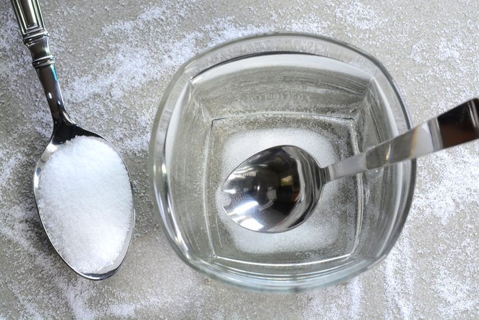 Preparing salt water, mixing table salt and a glass of hot water. Salt water is rich in minerals are used to treat cold and sore throat by gargling saltwater.