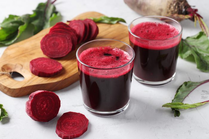 Two glass of fresh beetroot juice and chopped beet on wooden board on gray background. Closeup