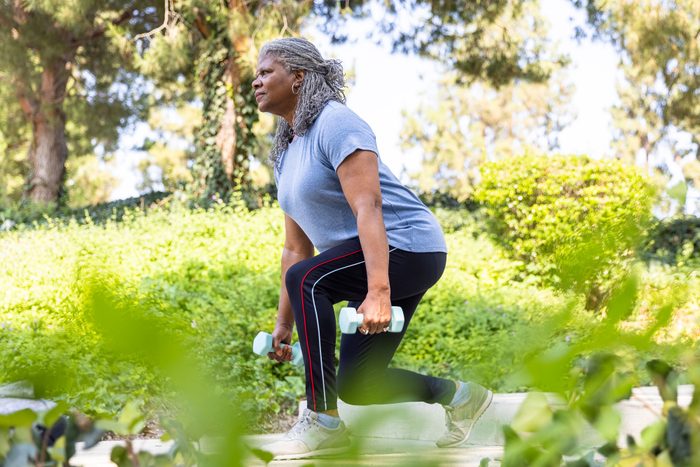 mature Black Woman doing lunges with handheld weights outdoors