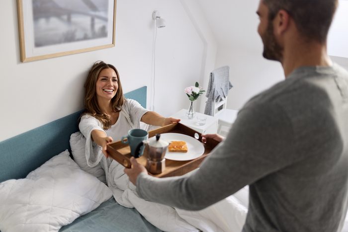 Loving man serving breakfast to beautiful woman in bed at home