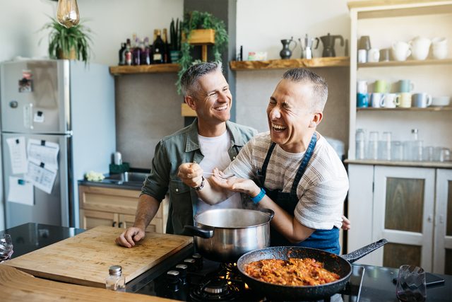 Mid adult cheerful gay couple talking and having fun while cooking in a kitchen