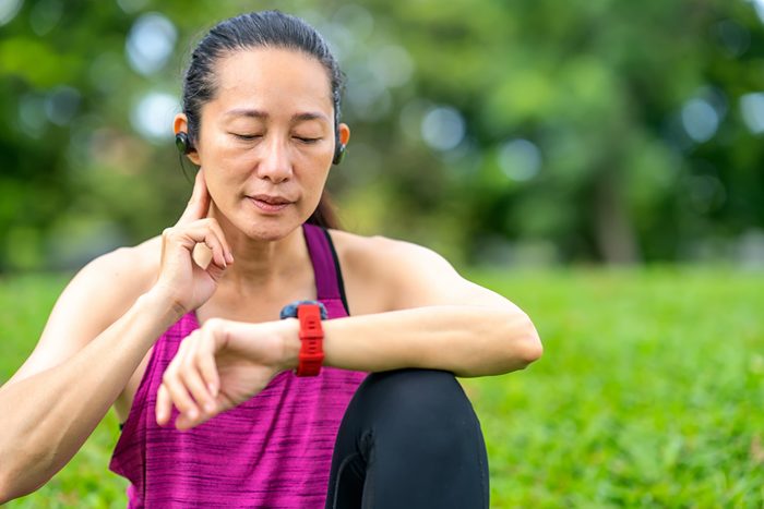 Asian women take their pulse and read data on a smartwatch after running outdoors at a public park. Outdoor exercise concepts.Measurement Heart Rate in Health Technology.