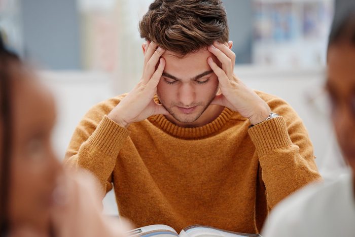 Study, stress and student at university with anxiety for a test. Young man with headache, worried and studying with textbook on desk in library. Tired in education, learning and stressed about exam