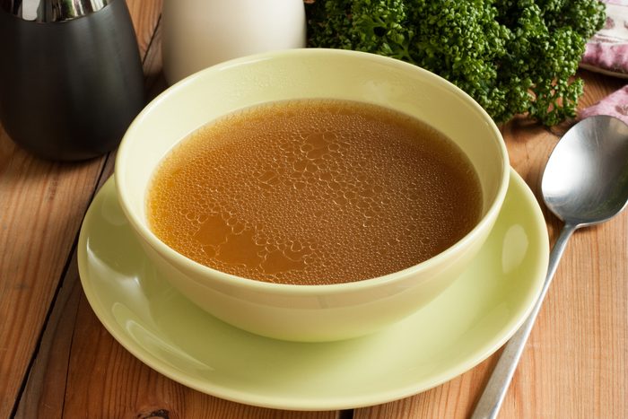 Bone broth in a yellow bowl on wood table