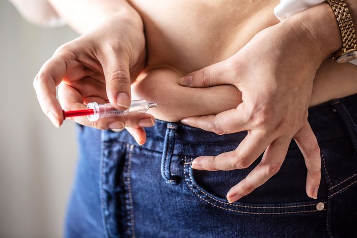 Woman holds her belly skin while applying insulin shot by an injection
