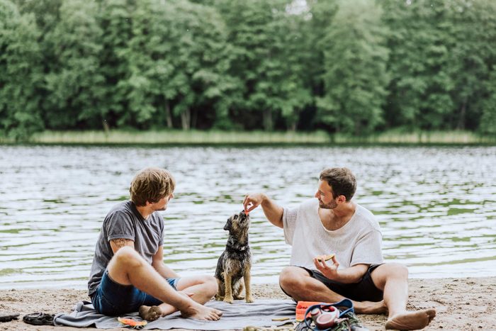 Two friends hanging out with their shared dog on a picnic blanket by a river