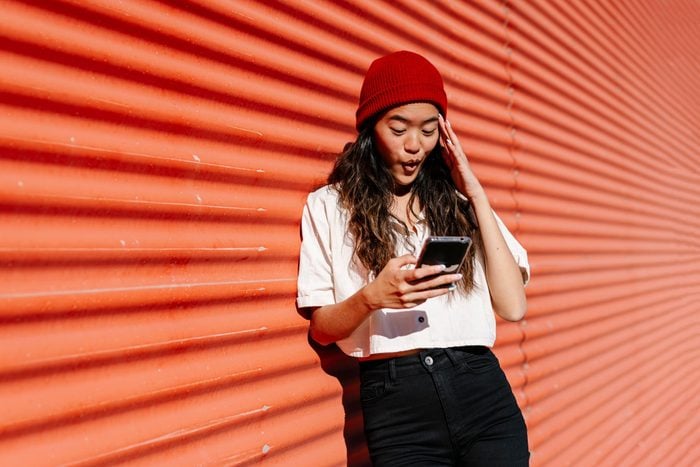 Surprised woman using mobile phone in front of corrugated wall
