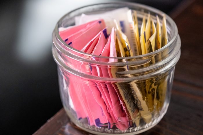 Assorted Artificial sweetener packets in a small glass bowl on a dark wooden table