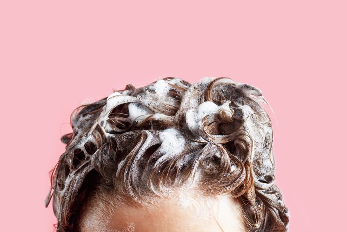 Female hair shampoo and foam on pink background close-up