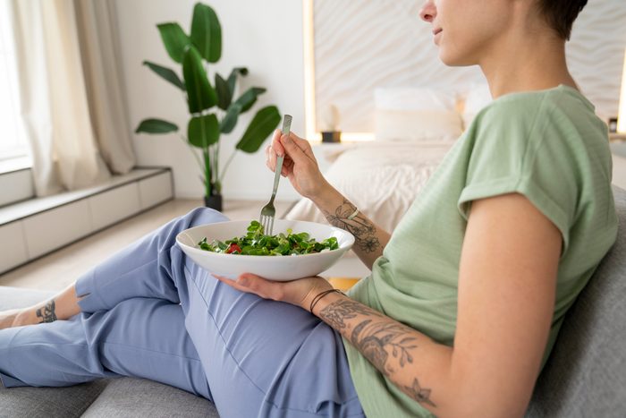Woman eating salad sitting on sofa at home