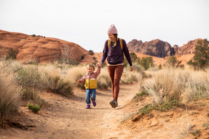 A mother and her daughter hiking a sandy foot path.
