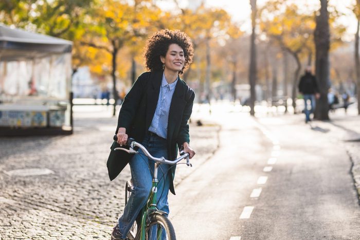 Beautiful woman with modern and relaxed look riding bike through park in autumn.