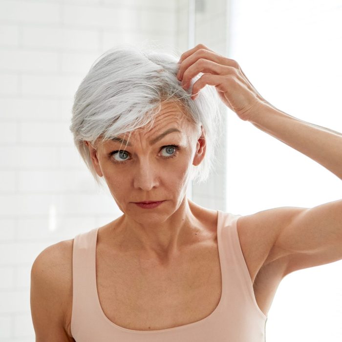 Adult woman looking at her gray hair in the mirror
