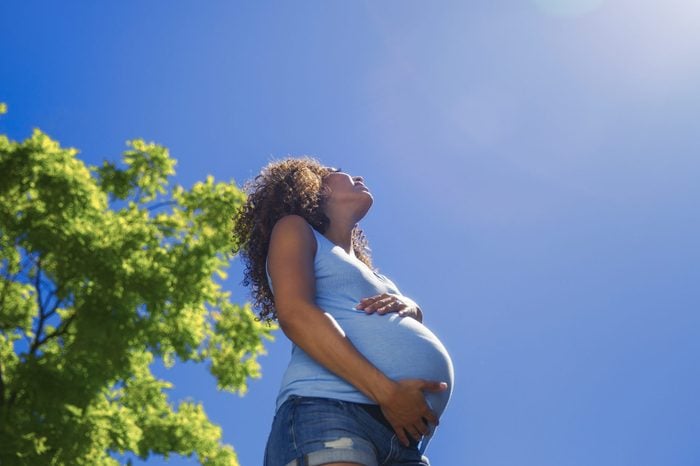 Mixed race pregnant lady holds bump on blue sky