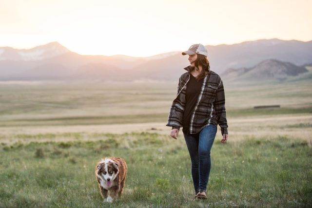 woman walking dog in a field with mountains in the background during sunset