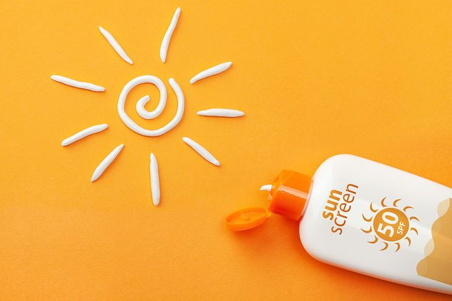Sunscreen On Orange Background with Plastic Bottle Of Sun Protection And White Sun Shaped Cream