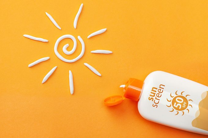 Sunscreen On Orange Background with Plastic Bottle Of Sun Protection And White Sun Shaped Cream