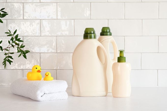 Eco Friendly Organic Laundry Detergent And Soap Gel Bottle With Branch Of Green Leaves, Towel And Yellow Duck On Table In Bathroom