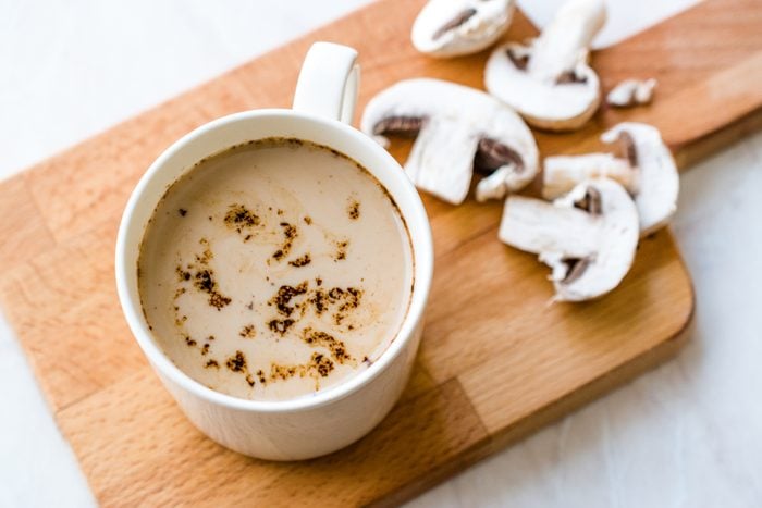 a mug of mushroom coffee on a wooden cutting board with sliced mushrooms I the background