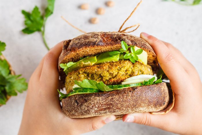 Vegan sandwich with chickpea patty, avocado, cucumber and greens in rye bread in children's hands.
