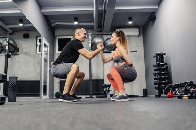 The concept of sports interesting and different fitness training. The couple does sports exercises together. They maintain balance by holding hands and doing squats, couple relationship goal