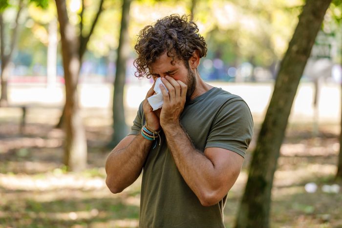 Man With Seasonal Flu is Walking in Park and Coughing in Paper Tissues.