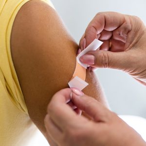Female doctor hands putting band-aid on woman arm after giving vaccine