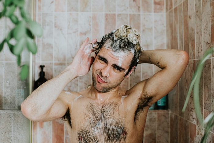 Portrait of a man washing his hair in the shower. He looks at the camera.