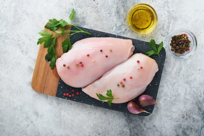 Chicken breast. Two Chicken fillet with spices, olive oil and parsley on black stone cutting board on grey stone table background. Top view with copy space. Food meat cooking background.