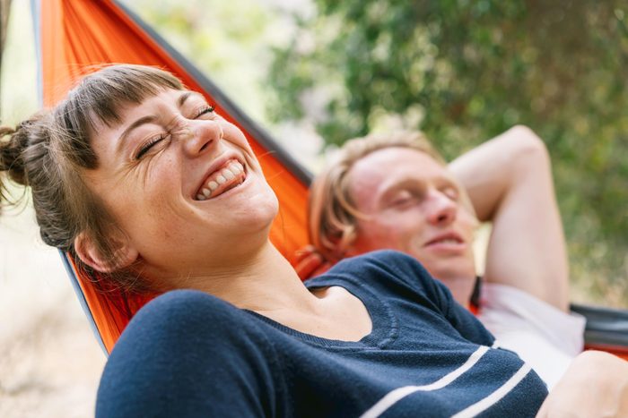 Young woman laughing while lying next to boyfriend in hammock