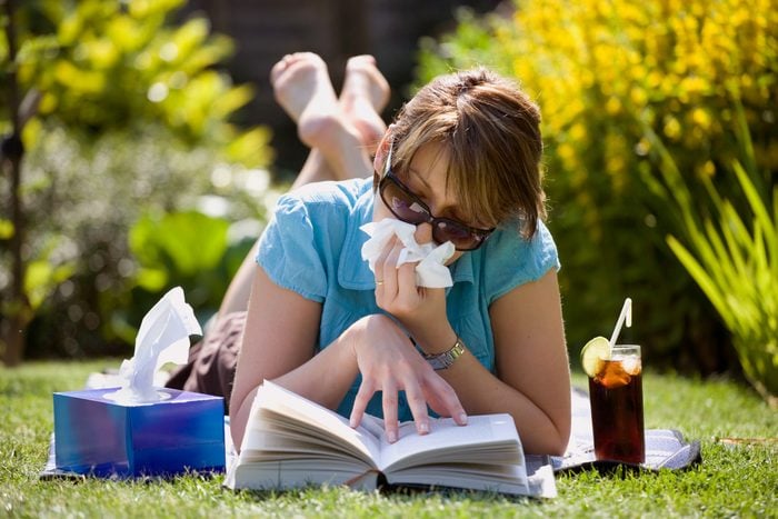 woman reading a book in the grass and blowing her nose