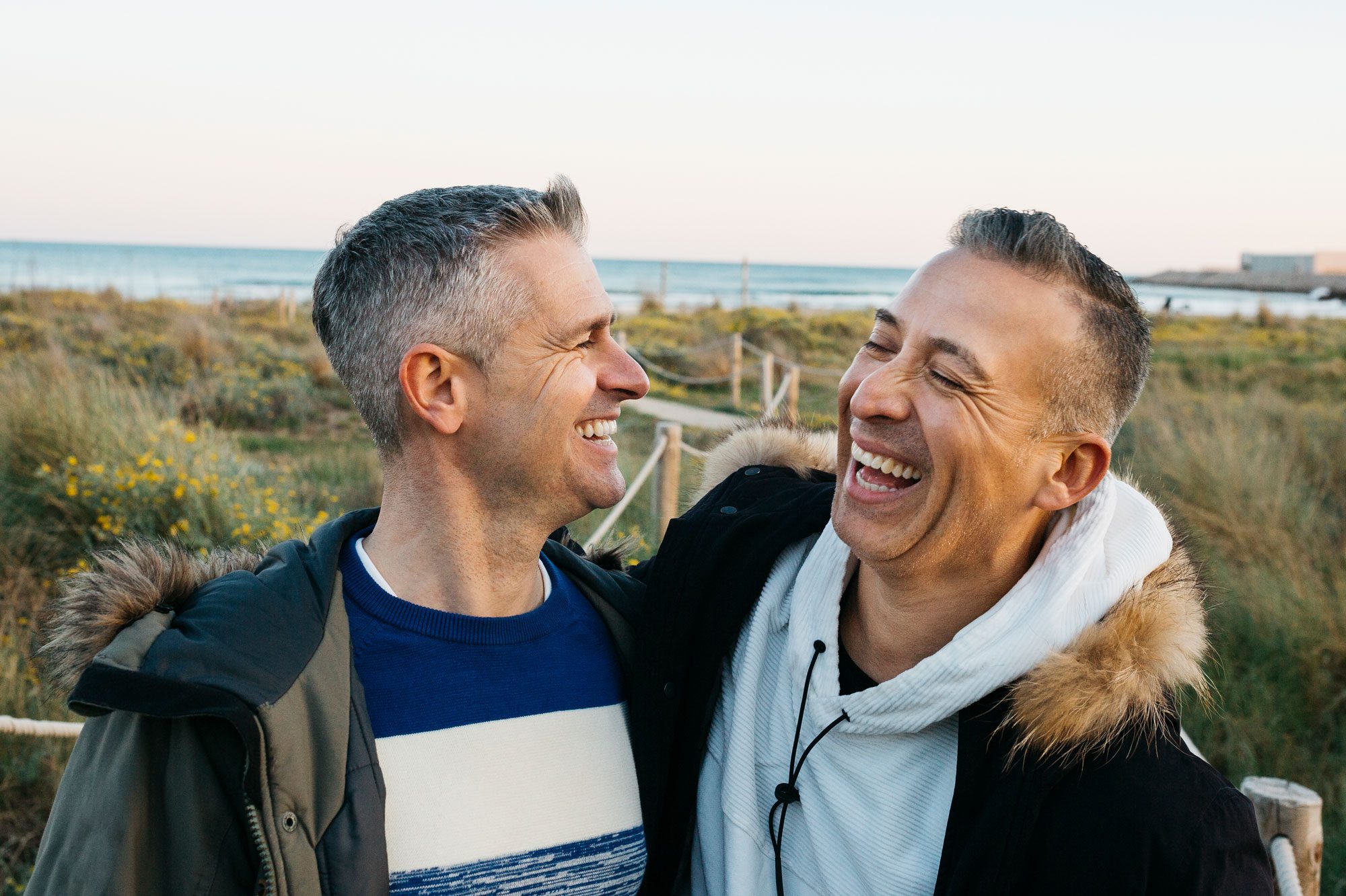 two men laughing near the beach during sunset