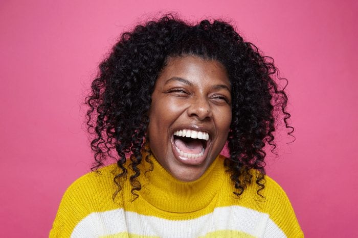Woman in yellow striped sweater Laughing against pink background