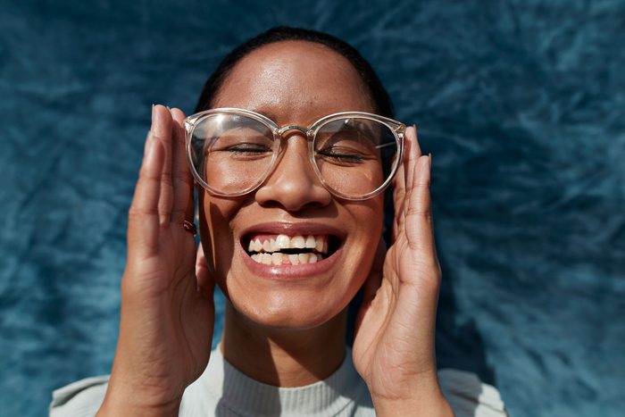 Laughing Woman Wearing Eyeglasses Against Blue Wall