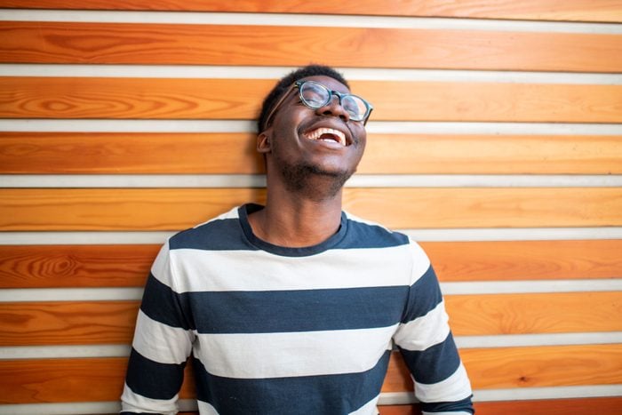 Young Black Man in a striped shirt and glasses Laughing against a wall with a striped wood pattern