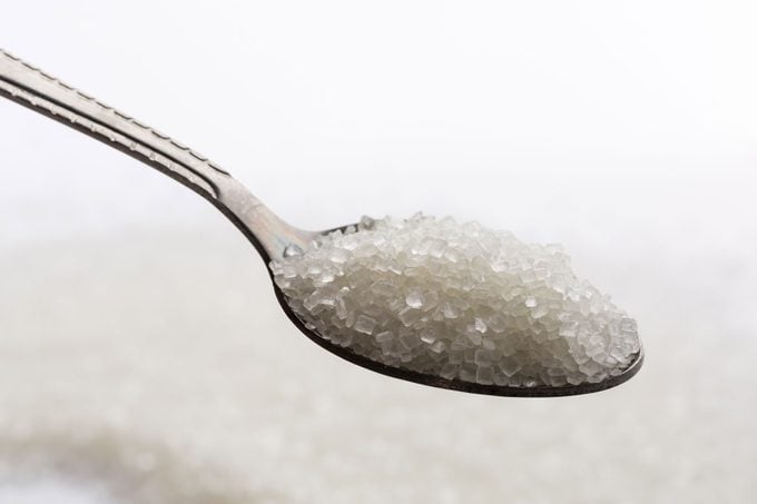 Sugar In A Spoon With sugar pile Background