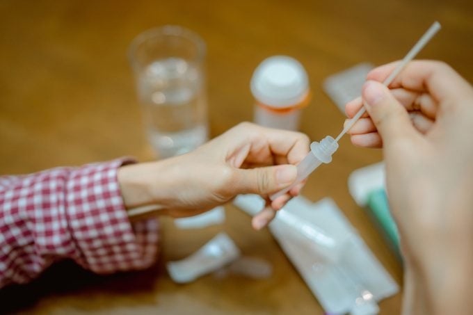 Asian woman drops swab in a protective plastic tube after nasal swab test to check for virus at home