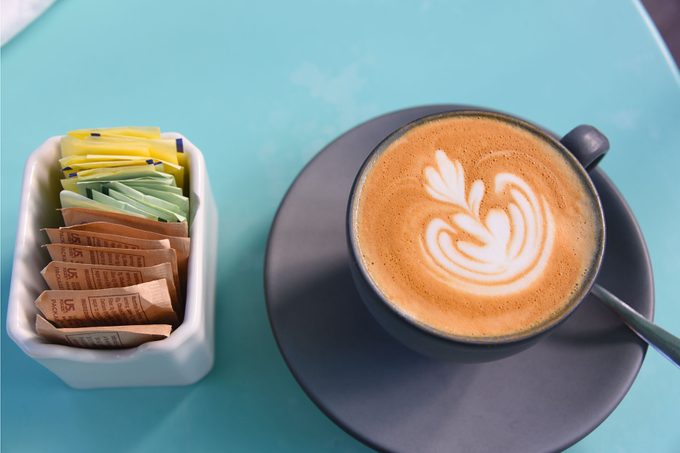 Overhead of a Cappuccino with fancy foam art and a sugar packet caddy on a blue background