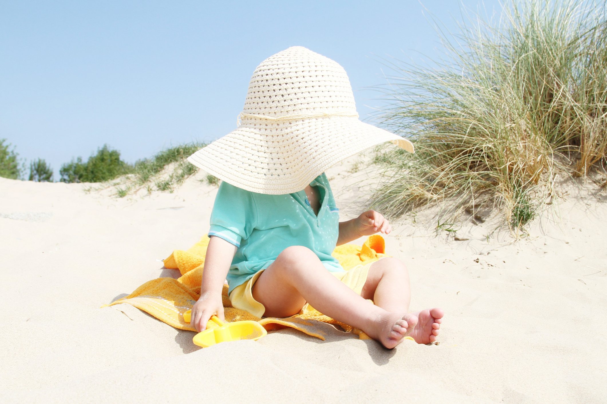 cute two year old boy on beach wearing large straw sunhat