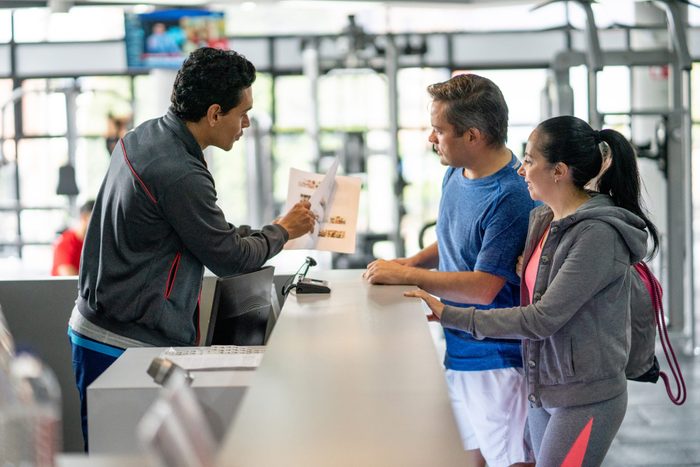 Happy couple registering at the gym while employee explains benefits showing them a catalogue