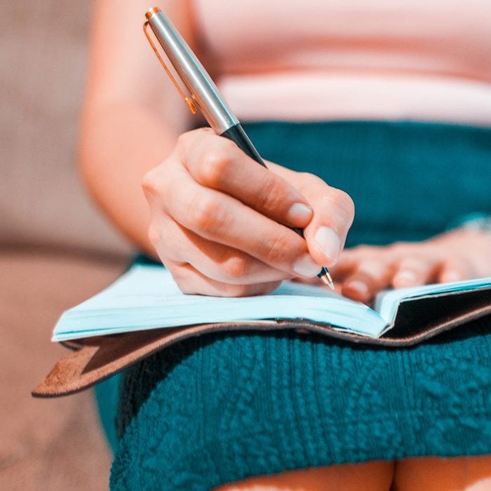 A young woman is writing on her journal while sitting on a couch