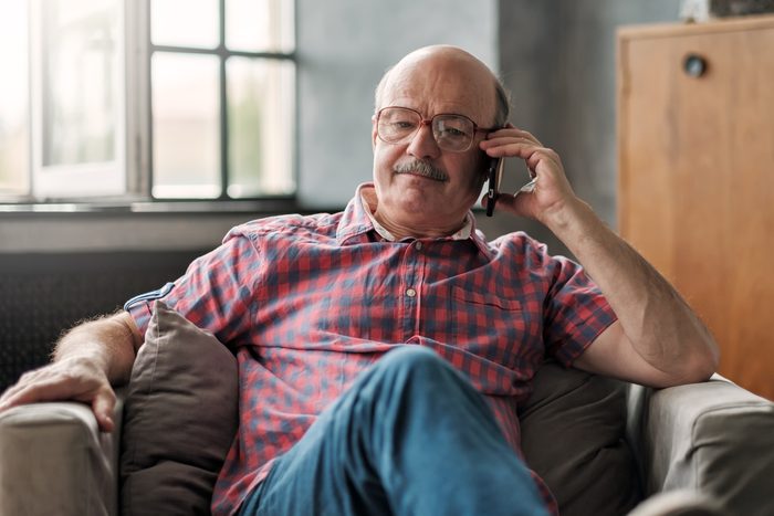 Retired hispanic man talking on phone sitting at living room.
