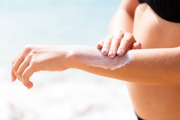 Pretty girl is putting sun lotion on her hand at the beach
