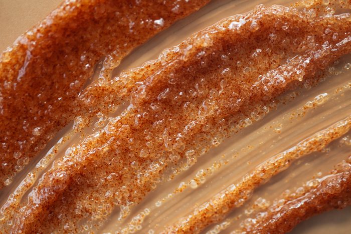 Texture of orange coffee and sugar scrub's smear with exfoliating particles on beige background. Concept of self-care and beauty treatment. Selfcare is a trendy procedure of the year. Cosmetics web banner