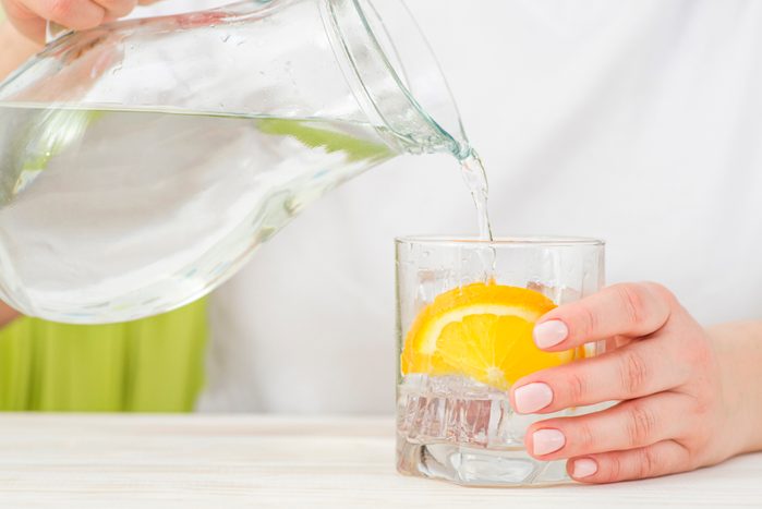 Female hands pouring water from the decanter into a glass beaker with lemon and ice after a massage