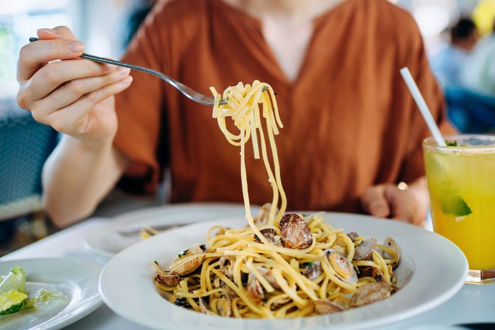 Close up of young Asian woman eating freshly served linguine pasta with fresh clams for lunch in a restaurant. Eating out lifestyle