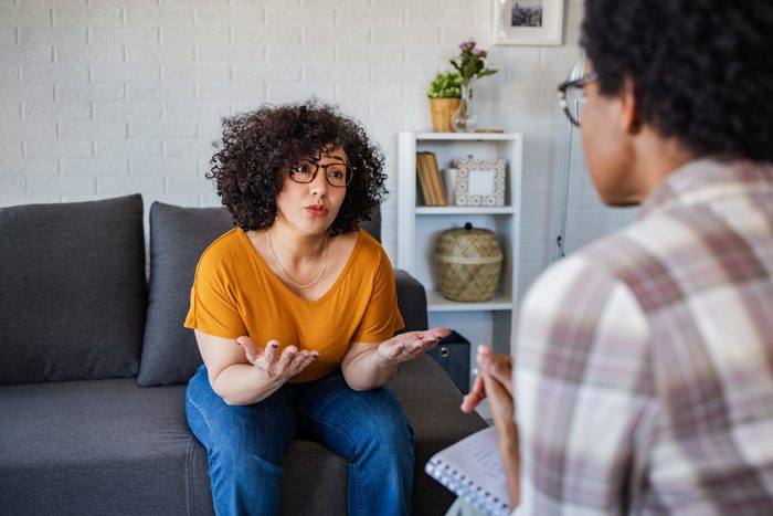 woman sitting on a grey couch and giving feedback to her therapist
